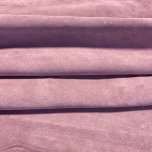 May include: A close-up of a soft, folded piece of mauve suede leather. The leather has a smooth, velvety texture.