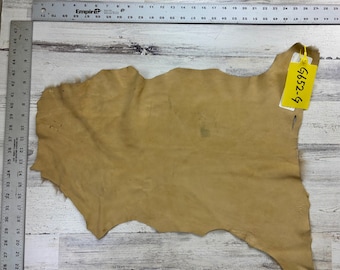 May include: A tanned leather hide with irregular edges, displayed on a light wood surface. A yellow tag with the text "G652-9" is attached to the hide. A metal ruler with inch markings is visible along the left edge.