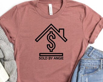 Peut inclure: Un t-shirt mauve avec un graphique noir d'une maison avec un signe dollar à l'intérieur et le texte "SOLD BY ANGIE" en dessous.