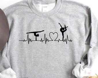 May include: Gray sweatshirt with a black graphic of a heart with two gymnasts in silhouette, one on the uneven bars and one in a handstand. The graphic is a heartbeat line.