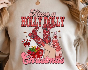 May include: A beige sweatshirt with the text "Have a Holly Dolly Christmas" in pink and red lettering. The design features a woman wearing red and white boots with a Christmas tree and presents.