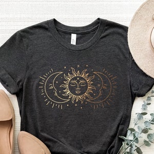 May include: A dark gray t-shirt with a gold sun and moon design. The sun has a face and the moon has a crescent shape.