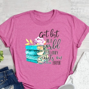 May include: A pink t-shirt with a graphic design of a stack of books with flowers and the text "Get lost in a world that only exists on paper".