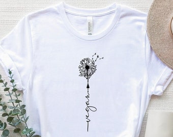 Op de afbeelding: Wit T-shirt met een zwarte paardenbloem afbeelding en het woord "vegan" verticaal eronder.