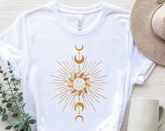 May include: White t-shirt featuring a gold sun and moon design. The sun has a face and is surrounded by rays. The moon is in a crescent shape and is repeated three times.