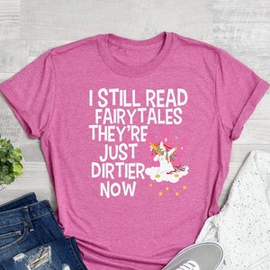 May include: Pink t-shirt with a white unicorn graphic and the text "I still read fairytales they're just dirtier now".
