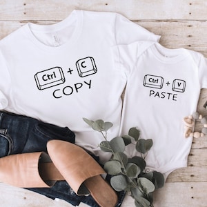 May include: White t-shirts with black text and keyboard icons. The larger shirt says "Ctrl + C COPY" and the smaller shirt says "Ctrl + V PASTE".