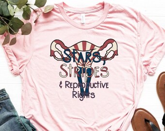 May include: Pink t-shirt with a graphic of a uterus with stars and stripes and the text "Stars & Stripes & Reproductive Rights".
