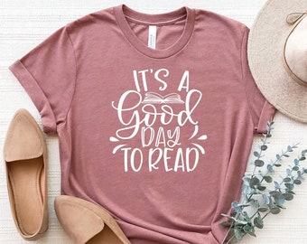 May include: A mauve t-shirt with the text "It's a good day to read" in white lettering. The text includes a stylized image of an open book.