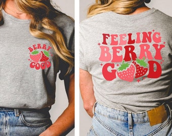 May include: A gray t-shirt with a red strawberry graphic and the text "Berry Good" on the front pocket. The back of the shirt has the text "Feeling Berry Good" in a retro font with a red strawberry graphic.