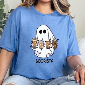 May include: A blue t-shirt featuring a white ghost holding various coffee drinks. The text "Boorista" is printed beneath the ghost.