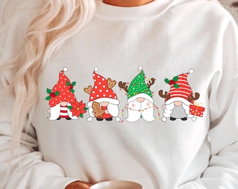 May include: White sweatshirt with a festive design featuring four gnomes wearing Santa hats and holding Christmas-themed items. The gnomes are lined up horizontally across the front of the sweatshirt.