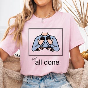May include: Light pink t-shirt with a graphic of hands and the words "(I'm) all done" in black. The shirt is made of a soft material and is suitable for casual wear. The design is simple and modern.