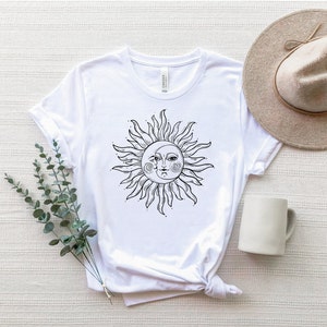 K&ouml;nnte beinhalten: Wei&szlig;es T-Shirt mit einem schwarzen und wei&szlig;en Sonnen- und Mondmotiv. Sonne und Mond sind stilisiert mit Gesichtern und haben eine sichelf&ouml;rmige Mondform.