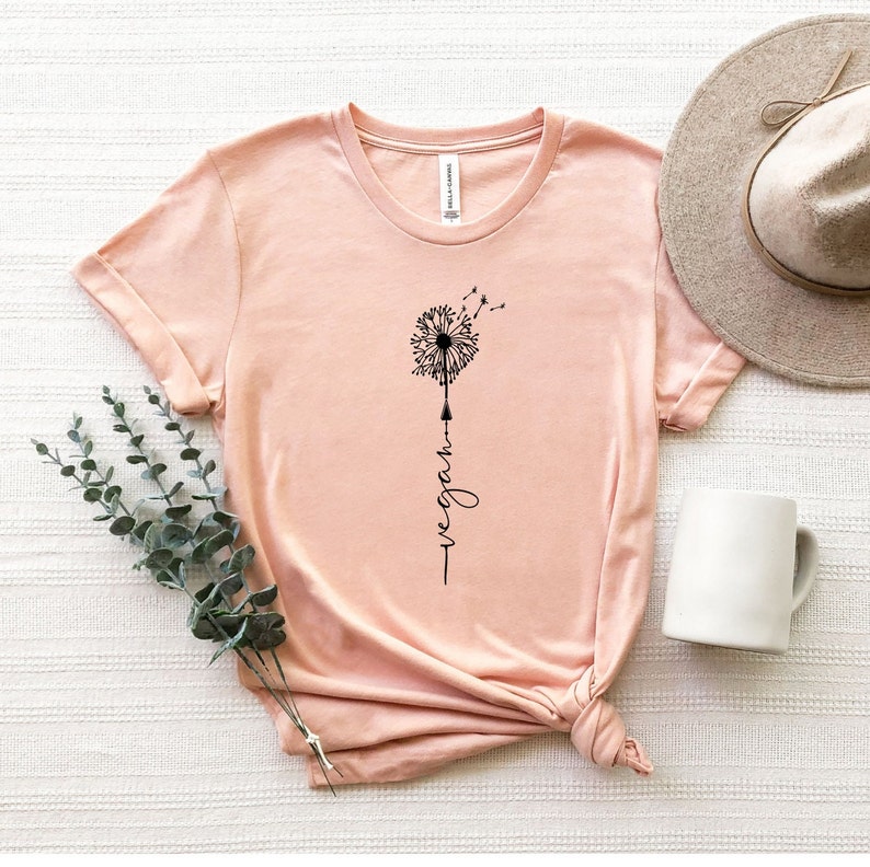 May include: A light pink t-shirt with a black dandelion graphic and the word "vegan" written vertically below it.