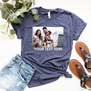 May include: A navy blue t-shirt with a photo of a family of three on a beach. The photo shows a man, a woman, and a young girl. The text "YOUR TEXT HERE" is printed below the photo.