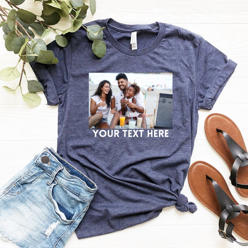 May include: A navy blue t-shirt with a photo of a family of three on a beach. The photo shows a man, a woman, and a young girl. The text "YOUR TEXT HERE" is printed below the photo.