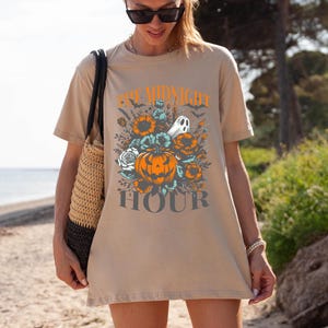 May include: A tan t-shirt with a graphic print of a pumpkin, flowers, and a ghost. The text "The Midnight Hour" is printed below the graphic.