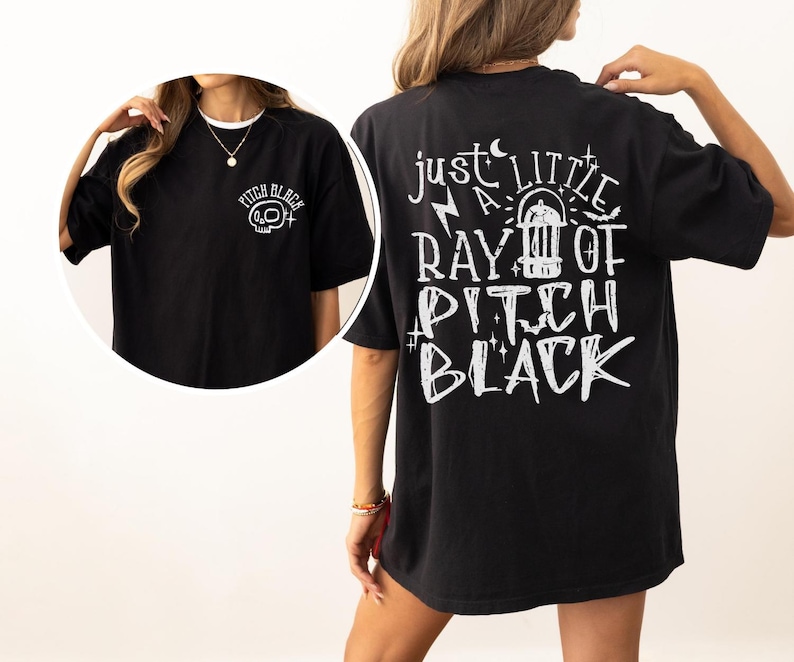 May include: Black t-shirt with white graphic text on the back that reads "just a little ray of pitch black." The front of the shirt has a small graphic of a skull and the words "pitch black."