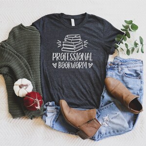 Peut inclure: Un t-shirt gris chin&eacute; fonc&eacute; avec un graphique de pile de livres et le texte "Professional Bookworm" en blanc.