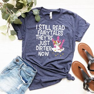 May include: A navy blue t-shirt with a white graphic of a unicorn doing the dab with the text "I still read fairytales they're just dirtier now".