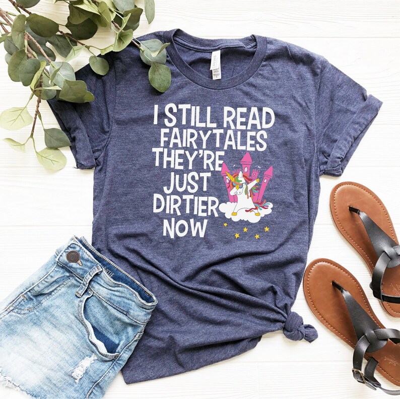 May include: A navy blue t-shirt with a white graphic of a unicorn doing the dab with the text "I still read fairytales they're just dirtier now".