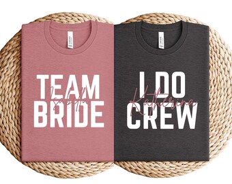 May include: Two t-shirts, one dusty rose and one charcoal, with white and pink text. The dusty rose shirt says "TEAM BRIDE" and the charcoal shirt says "I DO CREW". Both shirts are on a woven mat.