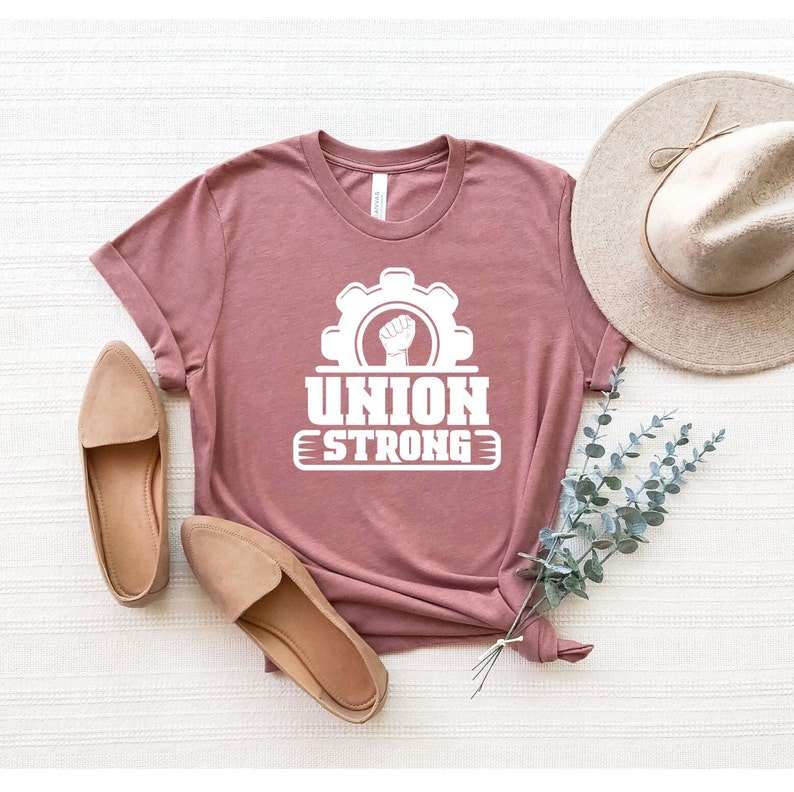 May include: A mauve t-shirt with a white graphic of a fist inside a gear with the text "UNION STRONG" underneath.