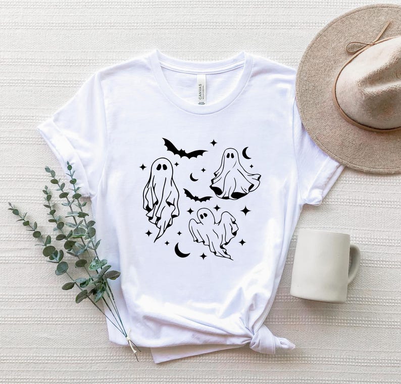 May include: White t-shirt with a black graphic of four ghosts and bats. The ghosts are in different poses and have a simple, minimalist design.