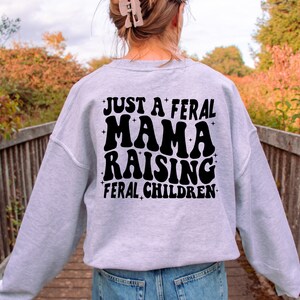 May include: Gray sweatshirt with black text that reads "Just a feral mama raising feral children".