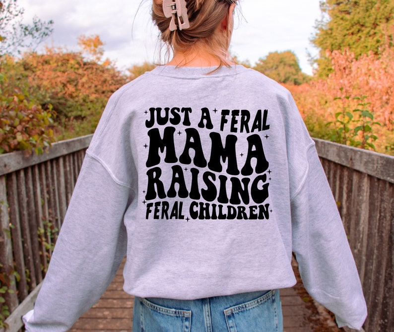 May include: Gray sweatshirt with black text that reads "Just a feral mama raising feral children".