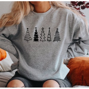 May include: A gray sweatshirt with a black design of five stylized Christmas trees. The trees are all different shapes and sizes, and some have stars on top.