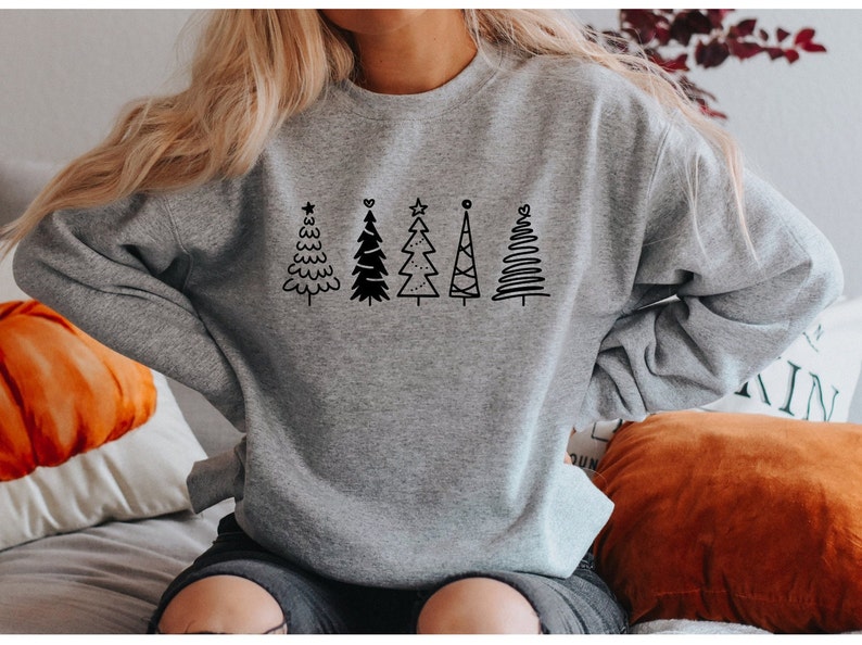 May include: A gray sweatshirt with a black design of five stylized Christmas trees. The trees are all different shapes and sizes, and some have stars on top.