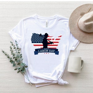 May include: White t-shirt with a graphic of a silhouette of a worker holding a hammer in front of an American flag in the shape of the United States. The text "Happy Labor Day" is printed below the graphic.