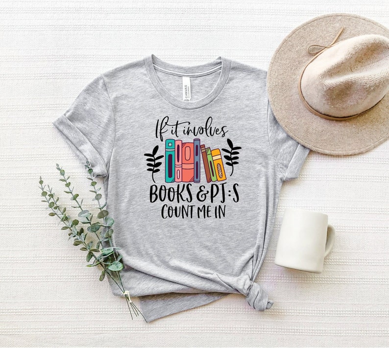 May include: A heather grey t-shirt with the text "If it involves books & pjs count me in" and a graphic of colorful books.