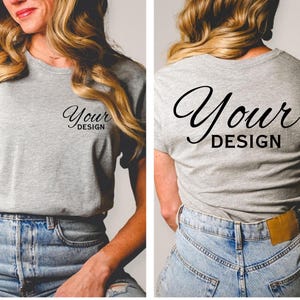 May include: A heather gray t-shirt with the words "Your Design" printed in black script on the front and back. The shirt has a crew neck and short sleeves. The model is wearing blue jeans.