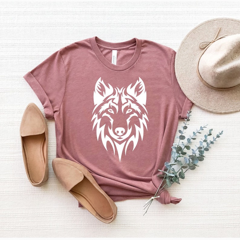 May include: A mauve t-shirt with a white wolf graphic design. The wolf is stylized with a tribal design.