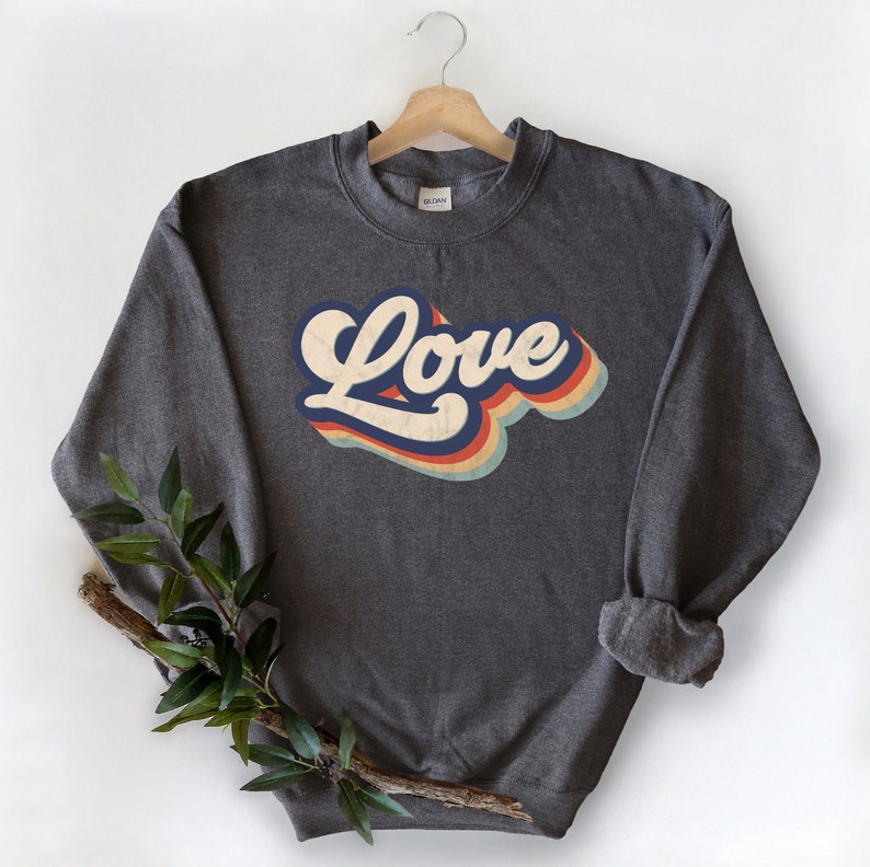 Puede incluir: Una sudadera gris oscuro con un gr&aacute;fico de "Love" de estilo retro en azul, naranja, amarillo y blanco.