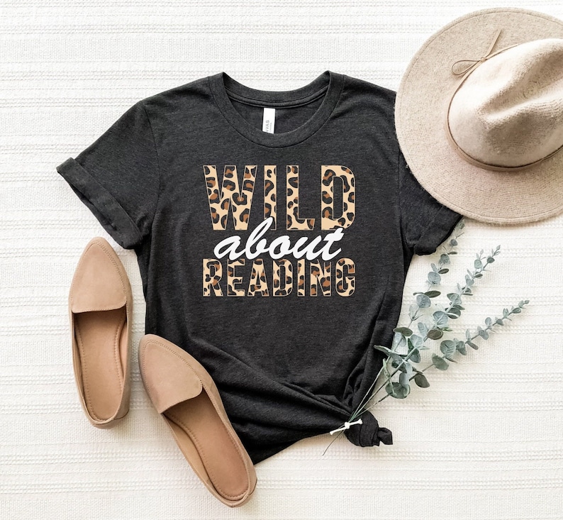 May include: A dark gray t-shirt with the text "WILD about READING" in white letters with a leopard print pattern.