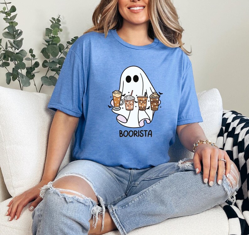 May include: A blue t-shirt featuring a white ghost holding various coffee drinks. The text "Boorista" is printed beneath the ghost.