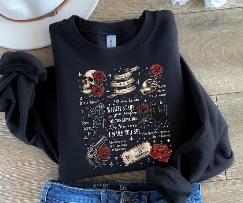 May include: Black sweatshirt with a graphic design featuring a skull, roses, a hand, a cat, and a gun. The design includes text that reads "Let me know which stars you prefer" and "House of Mirrors."