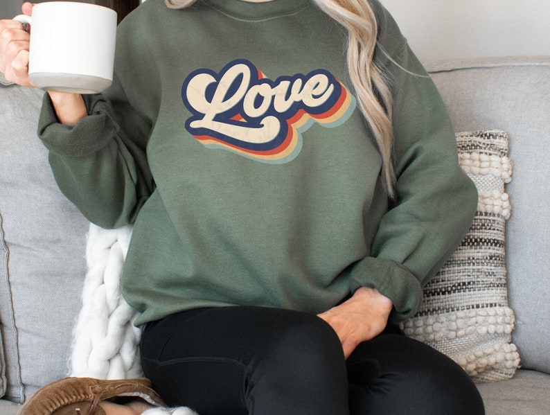 Puede incluir: Una sudadera verde con un gr&aacute;fico "Love" de estilo retro en naranja, amarillo, azul y rojo.