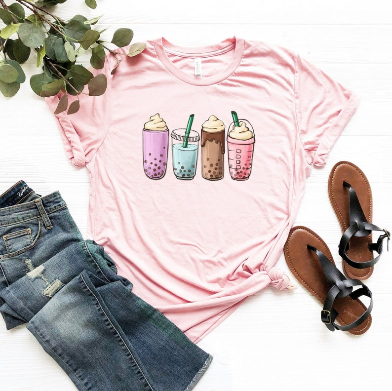 May include: Pink t-shirt with a graphic of four different boba tea drinks. The drinks are all in clear cups with colorful boba pearls and toppings.