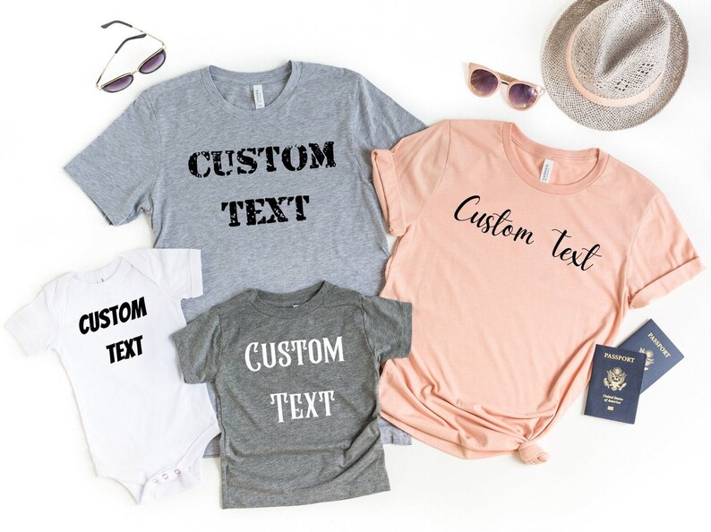 May include: Four t-shirts with the text "Custom Text" in different styles and colors. The shirts are laid out on a white surface.