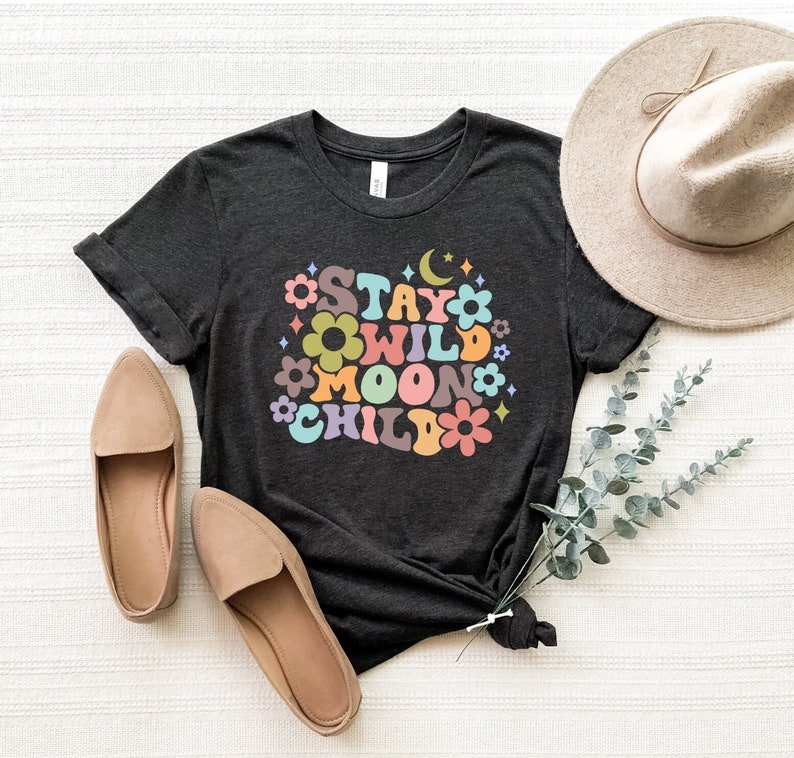 May include: A dark gray t-shirt with a colorful graphic that says "Stay Wild Moon Child" with flowers and stars surrounding the text.