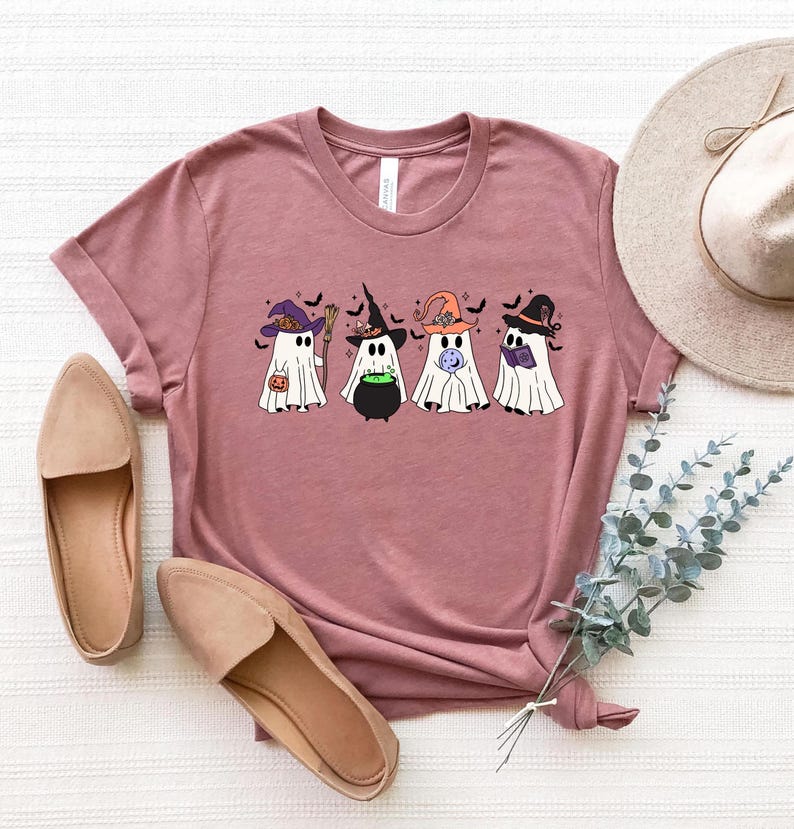Pu&ograve; includere: Una maglietta color malva con una grafica di cinque fantasmi che indossano cappelli da strega. I fantasmi tengono un calderone, una zucca, una luna e un libro. La grafica &egrave; in stile cartone animato.