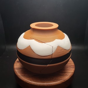 May include: A brown ceramic vase with a white and black design. The vase is sitting on a wooden base.