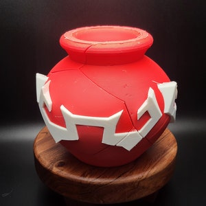 May include: A red ceramic pot with white geometric designs. The pot is round and has a wide opening at the top.