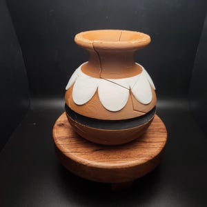 May include: A brown ceramic vase with a white and black design. The vase is sitting on a wooden base.