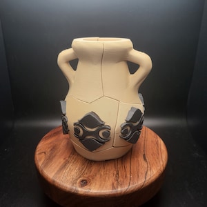 May include: A beige ceramic vase with a geometric design. The vase has two handles and is decorated with black geometric shapes.